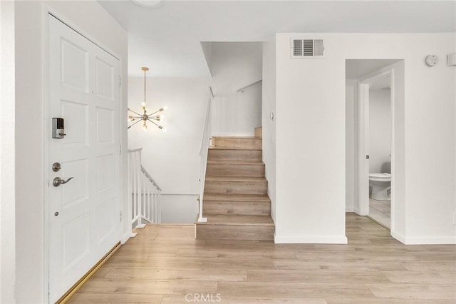 stairway featuring a notable chandelier, wood finished floors, visible vents, and baseboards