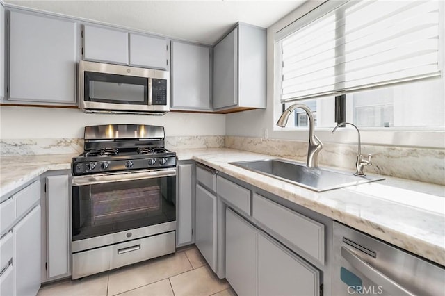 kitchen featuring light tile patterned floors, appliances with stainless steel finishes, a sink, and gray cabinetry