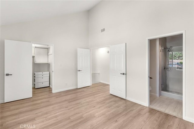 unfurnished bedroom with high vaulted ceiling, baseboards, a spacious closet, and light wood finished floors