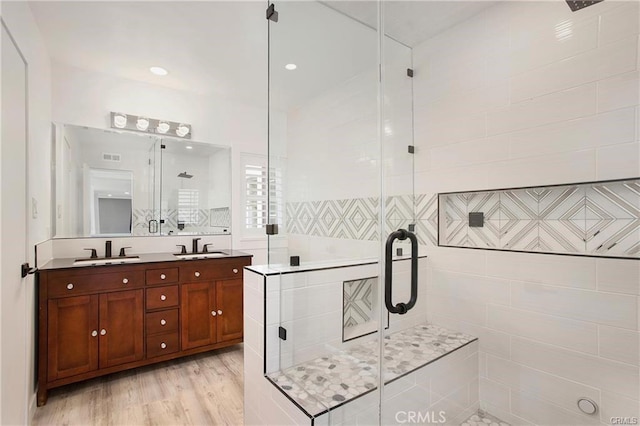 full bathroom featuring wood finished floors, a sink, a shower stall, and double vanity