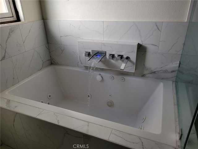 full bathroom featuring a textured wall and a tub with jets