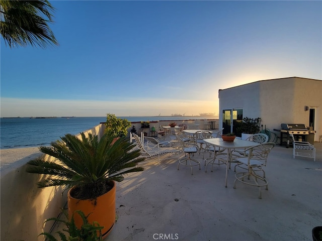 patio terrace at dusk featuring outdoor dining space, a water view, and grilling area