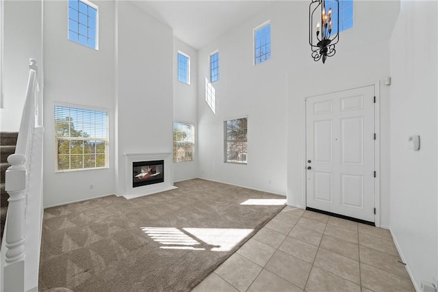 unfurnished living room with light tile patterned floors, light colored carpet, an inviting chandelier, a glass covered fireplace, and stairs