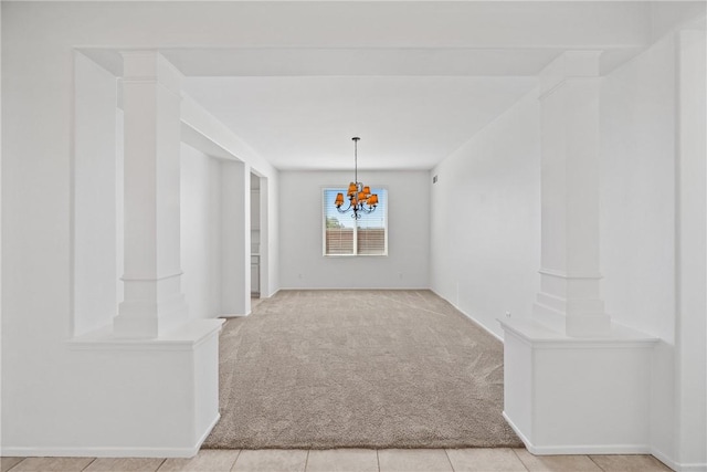 empty room featuring carpet floors, decorative columns, and a notable chandelier