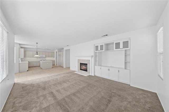 unfurnished living room with light carpet, visible vents, a fireplace, and a wealth of natural light