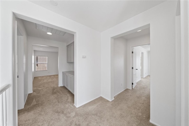 corridor featuring light colored carpet and baseboards