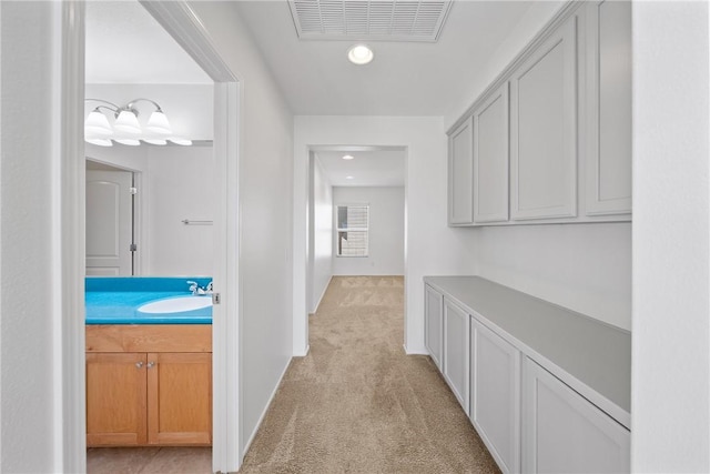 hall featuring light colored carpet, visible vents, and a sink