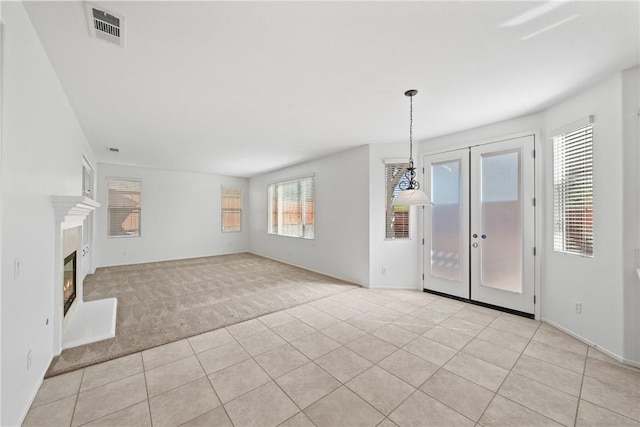 unfurnished living room with light carpet, light tile patterned floors, visible vents, a glass covered fireplace, and french doors