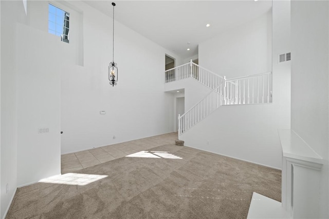 unfurnished living room featuring visible vents, a towering ceiling, stairway, tile patterned flooring, and carpet floors