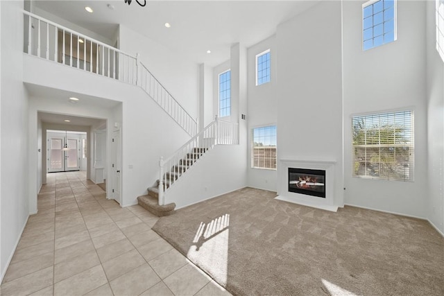 unfurnished living room with light carpet, light tile patterned floors, a glass covered fireplace, stairs, and recessed lighting