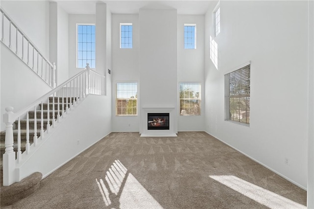 unfurnished living room with carpet floors, stairs, and a glass covered fireplace