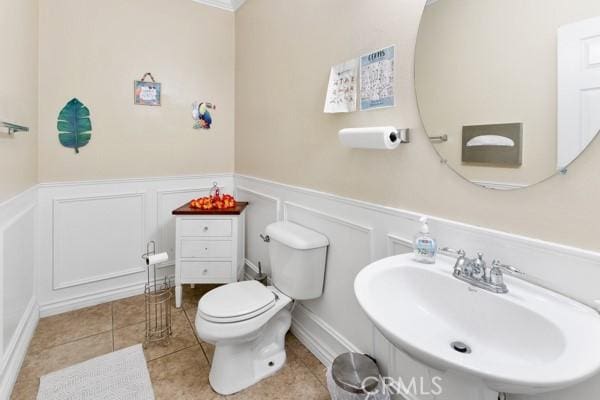 bathroom with toilet, wainscoting, a sink, and tile patterned floors