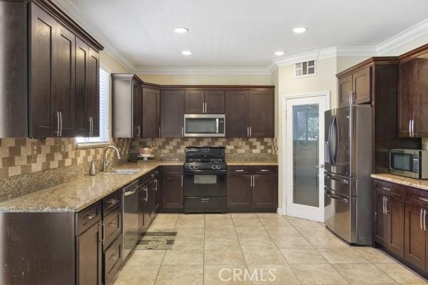 kitchen with stainless steel appliances, light stone counters, a sink, and crown molding