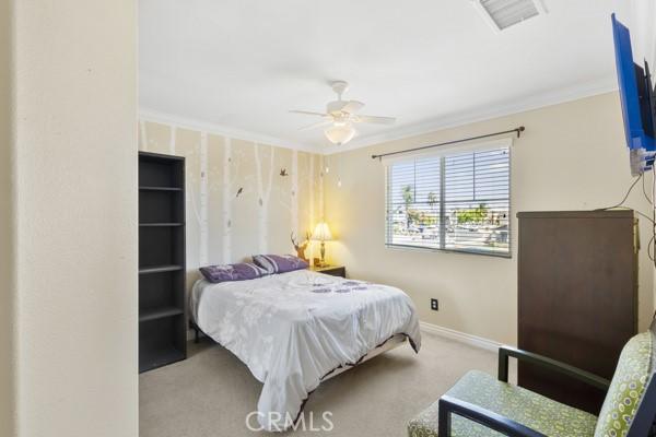 carpeted bedroom with ceiling fan, ornamental molding, visible vents, and baseboards