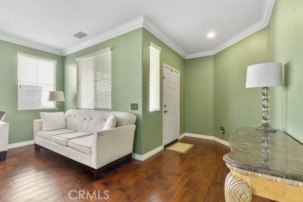 living room featuring ornamental molding, visible vents, baseboards, and hardwood / wood-style flooring