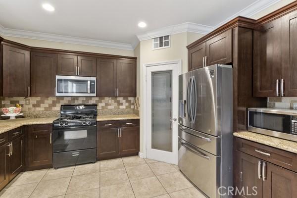 kitchen with light tile patterned flooring, dark brown cabinetry, stainless steel appliances, visible vents, and ornamental molding