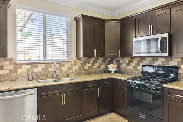 kitchen with a sink, dark brown cabinets, appliances with stainless steel finishes, decorative backsplash, and crown molding