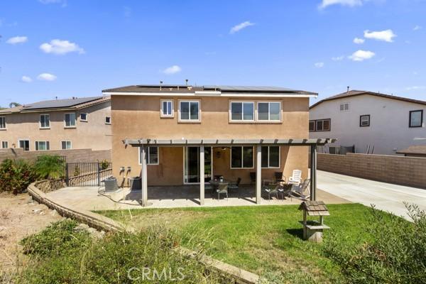 back of house with a fenced backyard, solar panels, a lawn, stucco siding, and a patio area