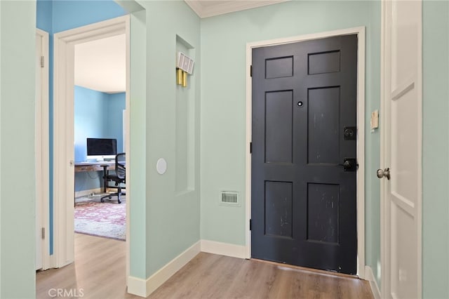 entryway with baseboards, visible vents, wood finished floors, and crown molding