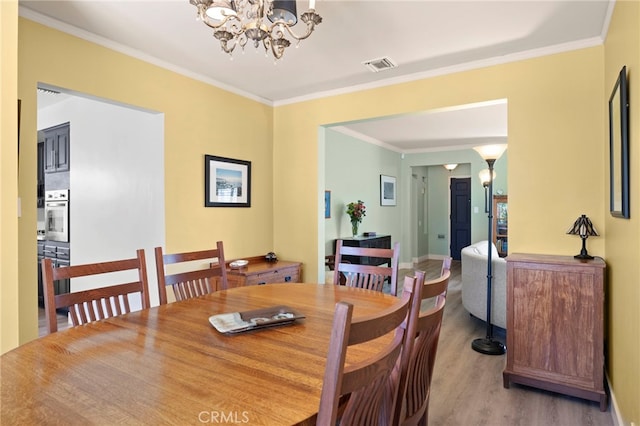 dining space featuring crown molding, visible vents, a chandelier, baseboards, and wood finished floors
