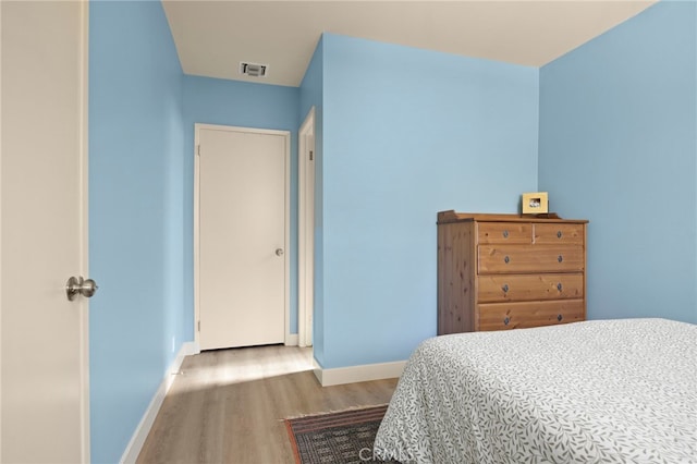 bedroom with baseboards, visible vents, and wood finished floors