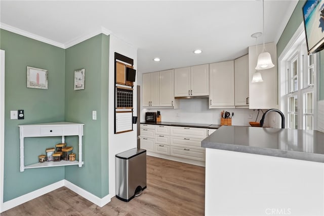 kitchen with dark countertops, hanging light fixtures, light wood-style floors, white cabinets, and baseboards