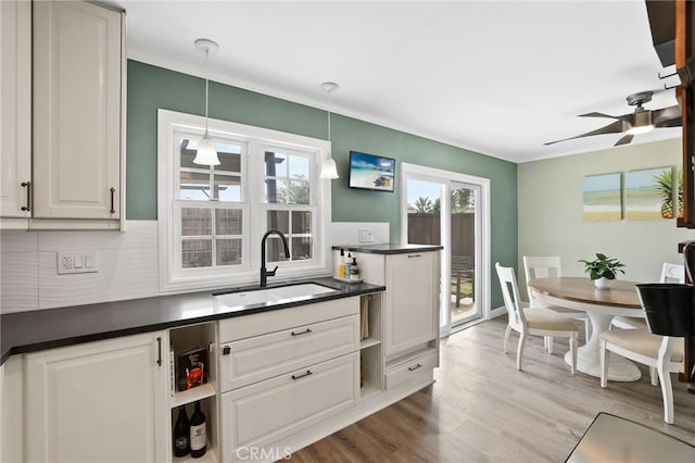 kitchen with dark countertops, wood finished floors, decorative light fixtures, white cabinetry, and a sink