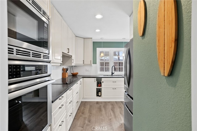 kitchen with stainless steel appliances, a sink, white cabinetry, light wood finished floors, and dark countertops