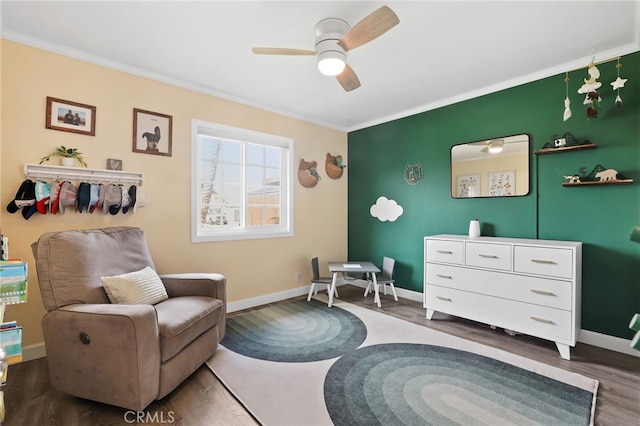 living area with baseboards, wood finished floors, a ceiling fan, and crown molding