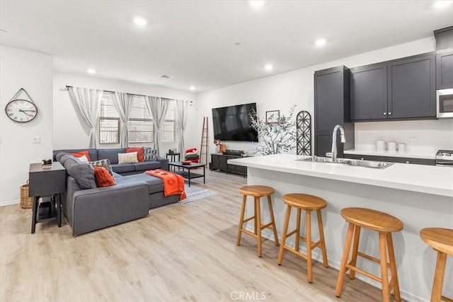 kitchen featuring stainless steel appliances, a breakfast bar, a sink, light countertops, and light wood finished floors