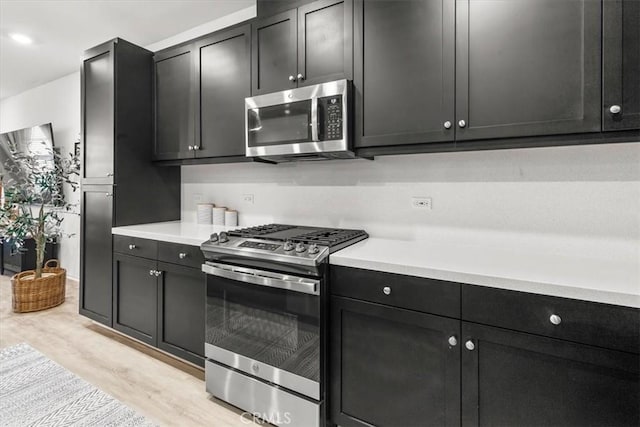 kitchen featuring stainless steel appliances, light wood finished floors, light countertops, and dark cabinets