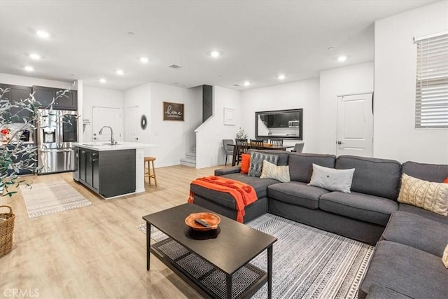 living room featuring light wood-type flooring, visible vents, recessed lighting, and stairs