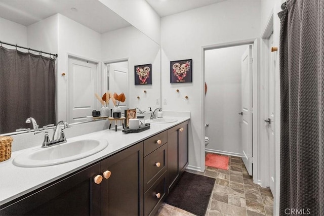 bathroom with toilet, stone finish flooring, double vanity, and a sink