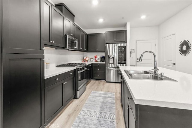 kitchen with appliances with stainless steel finishes, light wood-type flooring, light countertops, and a sink