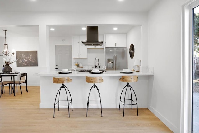 kitchen with a kitchen bar, island exhaust hood, light wood finished floors, and stainless steel fridge with ice dispenser