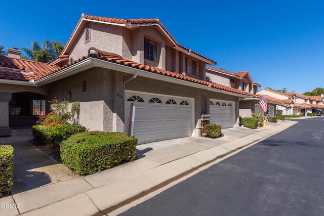 view of front of house with a tile roof, a chimney, stucco siding, a garage, and driveway