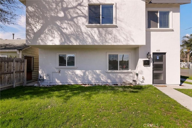 back of house featuring a yard, fence, and stucco siding