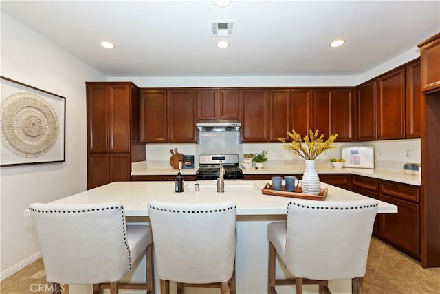 kitchen featuring stainless steel gas range oven, visible vents, a breakfast bar area, under cabinet range hood, and recessed lighting