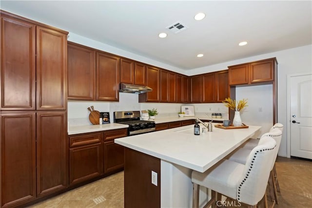 kitchen with visible vents, light countertops, under cabinet range hood, a sink, and gas stove