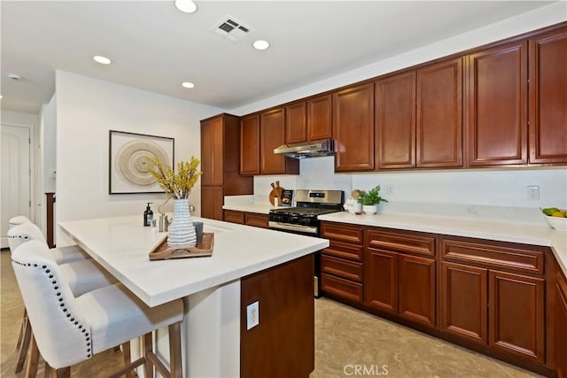 kitchen with visible vents, gas stove, a kitchen breakfast bar, under cabinet range hood, and recessed lighting