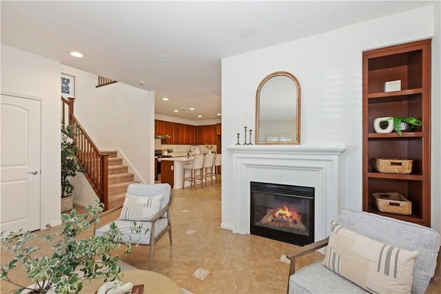 living room with built in features, a glass covered fireplace, stairway, and recessed lighting