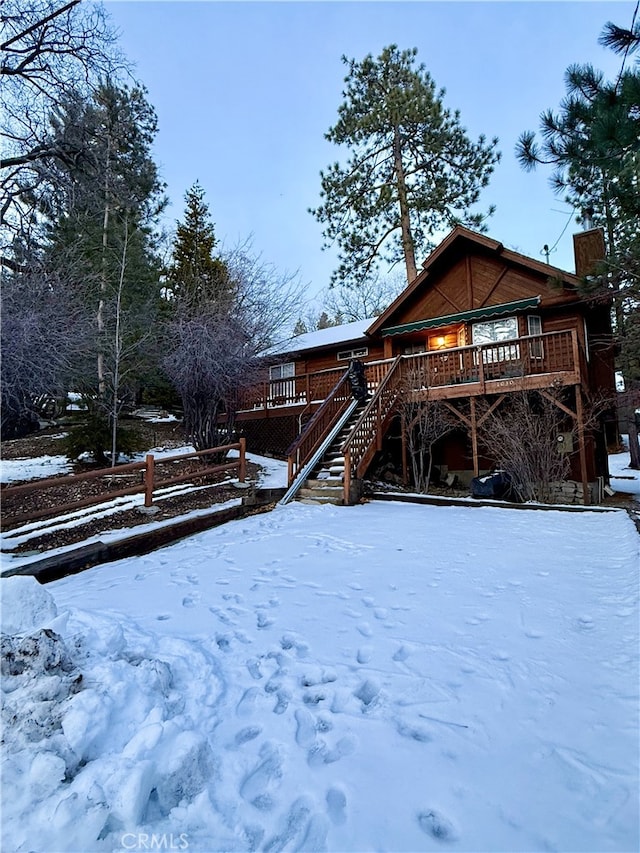 snow covered rear of property with stairway and a deck