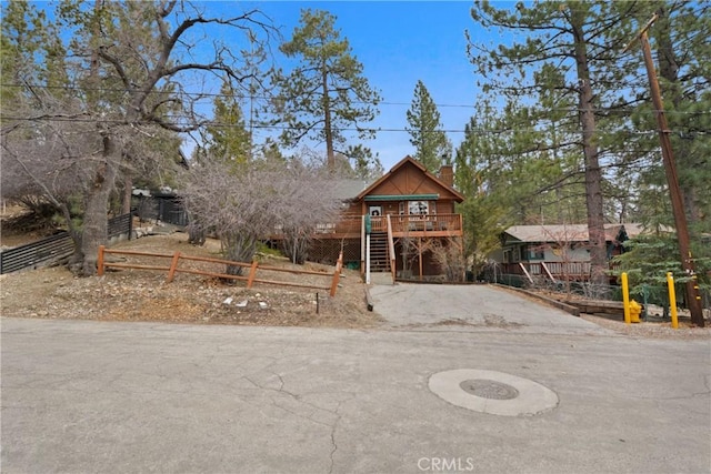 rustic home featuring a chimney, stairway, fence, a deck, and driveway