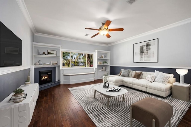 living room featuring visible vents, ornamental molding, ceiling fan, wood finished floors, and a warm lit fireplace