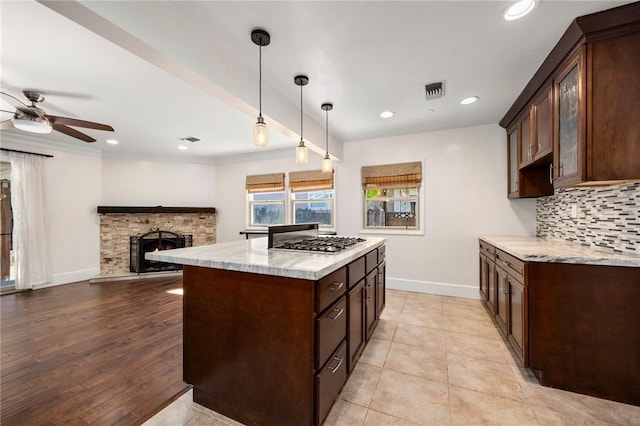 kitchen featuring tasteful backsplash, baseboards, dark brown cabinets, a stone fireplace, and stainless steel gas stovetop