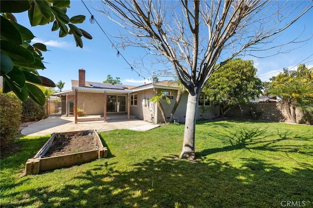 back of house with a patio, a fenced backyard, a lawn, roof mounted solar panels, and a chimney