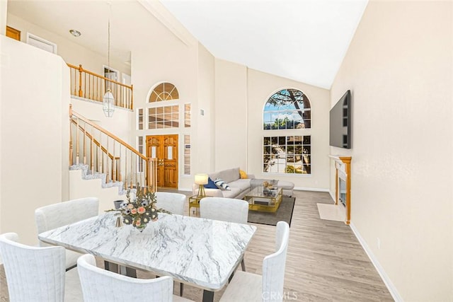 dining area with high vaulted ceiling, stairway, wood finished floors, and baseboards