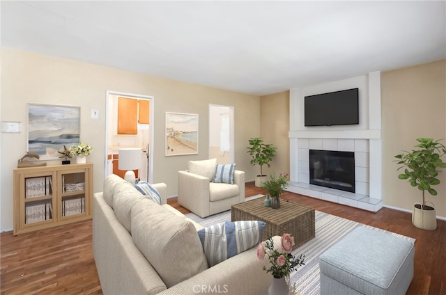 living room with a tiled fireplace, baseboards, and wood finished floors