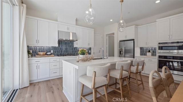 kitchen with tasteful backsplash, light countertops, appliances with stainless steel finishes, white cabinets, and under cabinet range hood