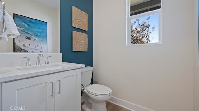 half bath with baseboards, vanity, toilet, and wood finished floors